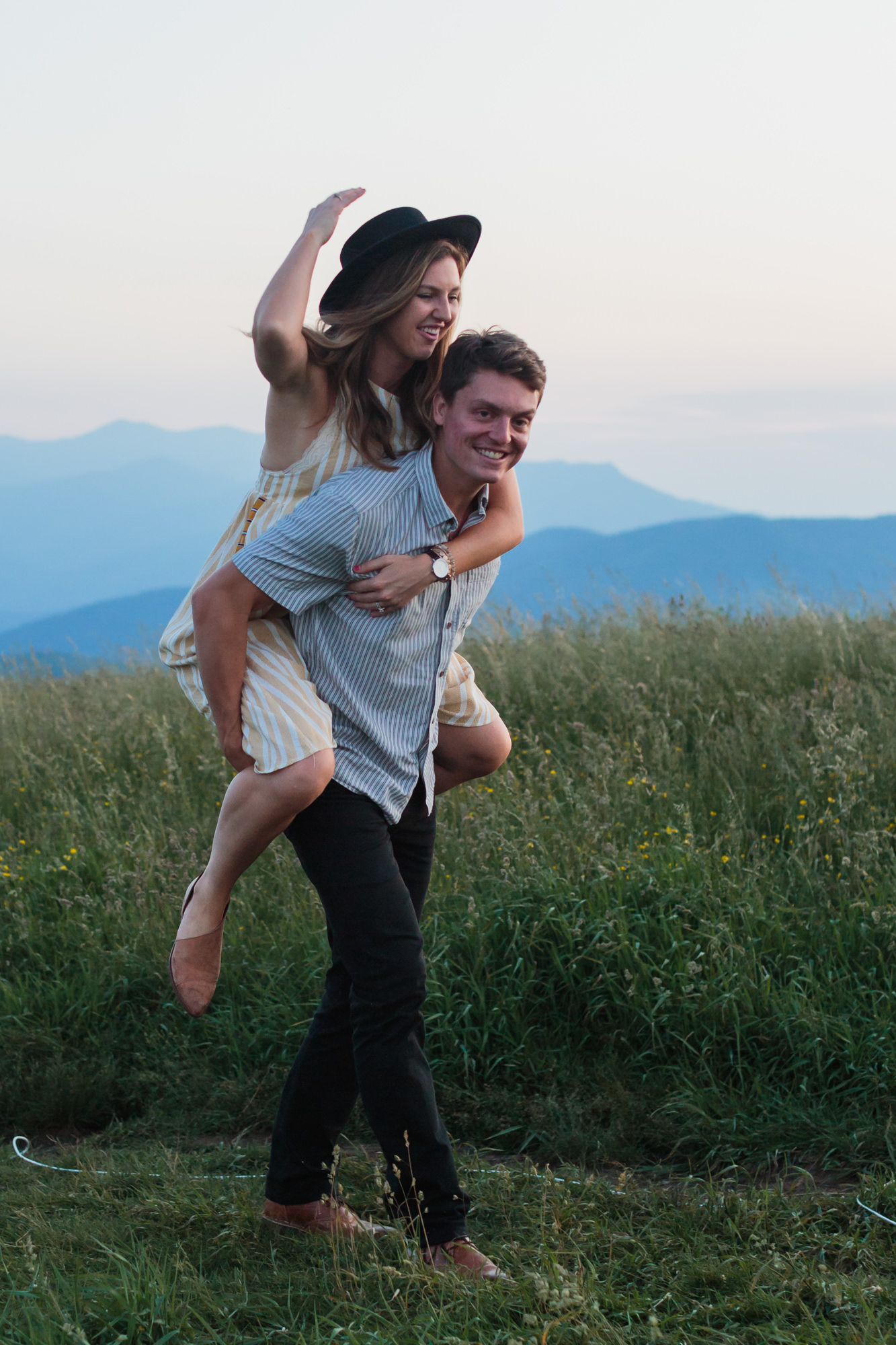 date night guy giving piggyback ride while girl holds onto hat, Nashville engagement, couples mountain, mountain engagement, couples camping, dog photography, Knoxville, couples hiking, camping with dog, North Carolina hiking, summer engagement photos, Tennessee Photography, Tennessee Photographer, Tennessee Photos, Tennessee Engagement Photography, Tennessee Engagement Photos, Tennessee Engagement Photographer, Tennessee Portrait Photographer, Nashville Engagement Photographer, Nashville Engagement Photos, Knoxville Engagement, Nashville Lifestyle Photographer, Nashville Lifestyle Photography, Nashville Lifestyle Photos, Creative Portraits
